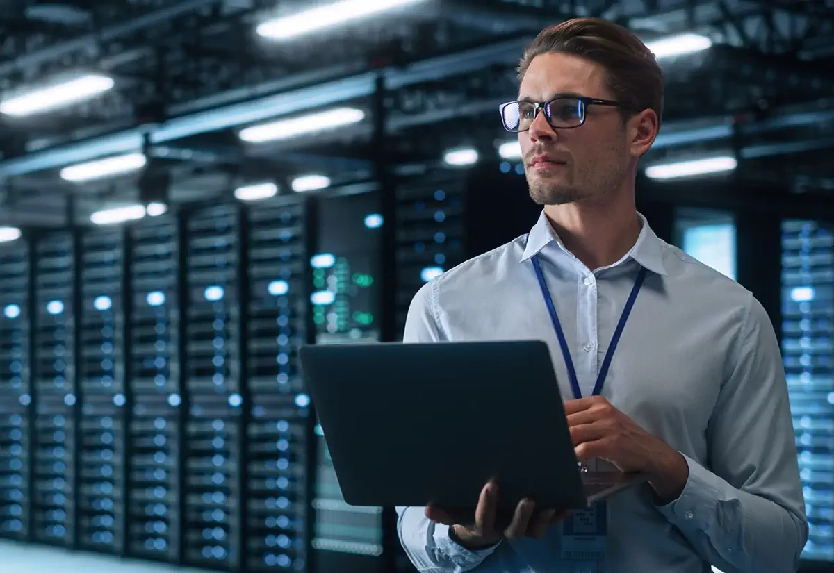 IT specialist with a laptop in a data center – managing servers and IT infrastructure security.