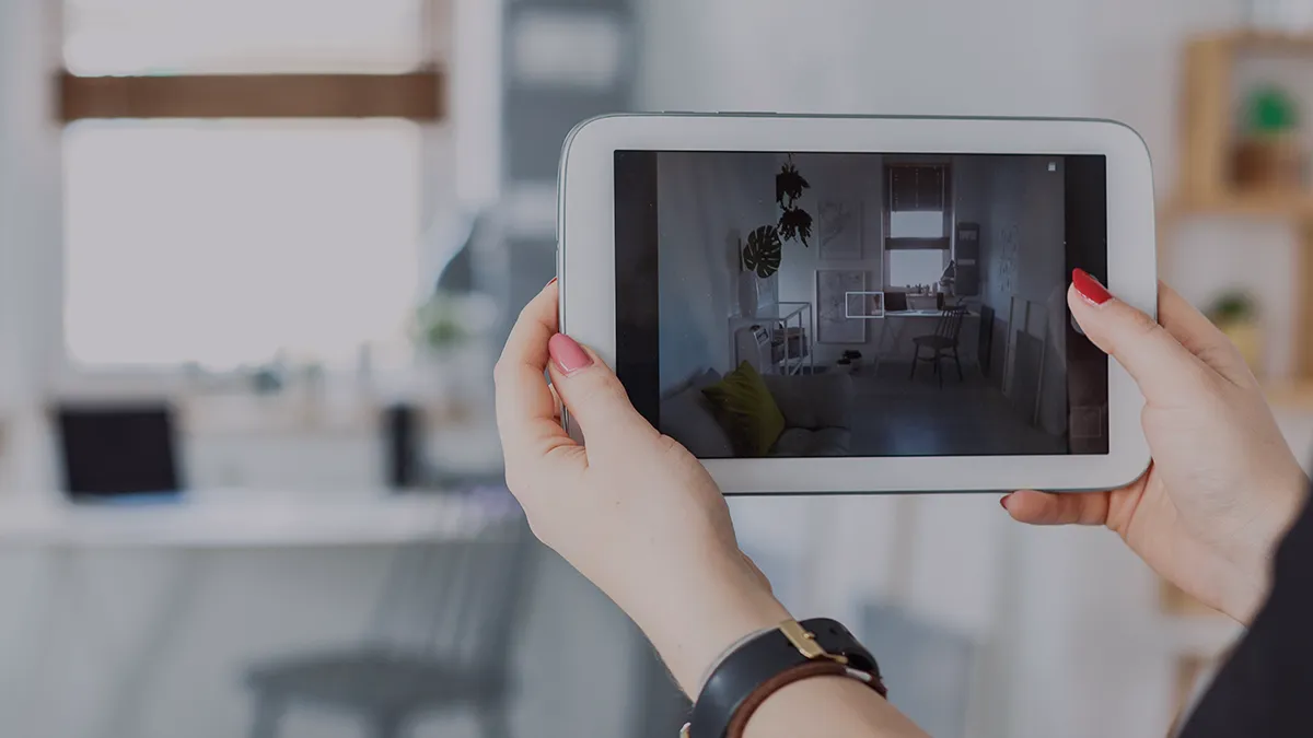 Das Foto zeigt die Hände einer Frau, die ein Tablet hält. Der Rahmen ist auf dem Bildschirm des Geräts zentriert - er zeigt einen Raum, auf den die Kamera des Tablets gerichtet ist, wobei die Mitte des Rahmens markiert ist. Aus dem Kontext geht hervor, dass die Frau das Foto des Raums verwenden wird. Das Foto ist die Titelgrafik für eine Erfolgsgeschichte von Transition Technologies PSC mit dem Titel: Effektive Nutzung von AR zur Fensterabdeckungs-Anordnung und -Dimensionierung.