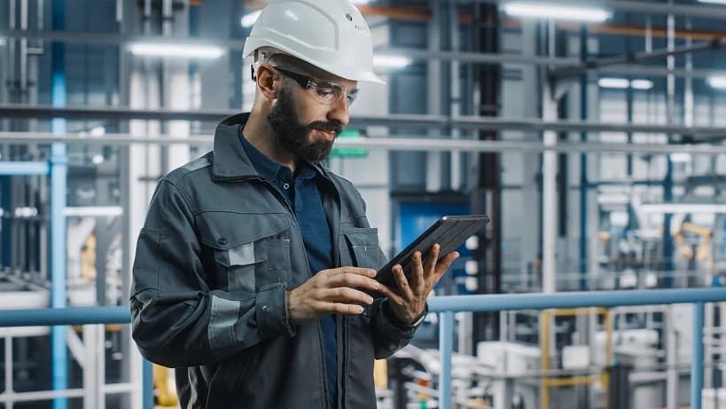 Engineer wearing a safety helmet using a tablet in a modern manufacturing facility.