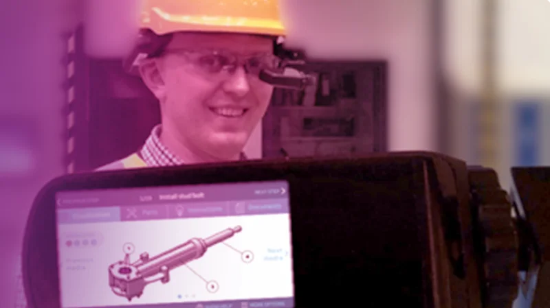 Two colleagues work together at a computer, with one pointing at the screen.