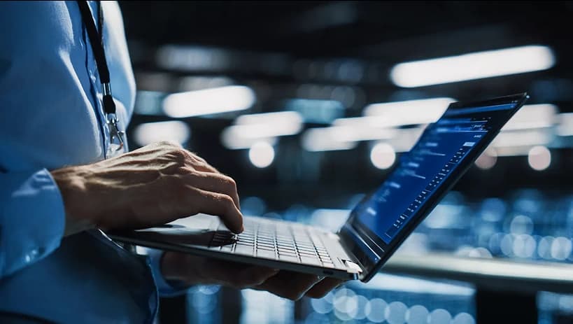 Specjalista IT korzystający z laptopa w nowoczesnej serwerowni, symbolizujący oparte na chmurze zarządzanie cyklem życia produktu (PLM) i cyfrową transformację.