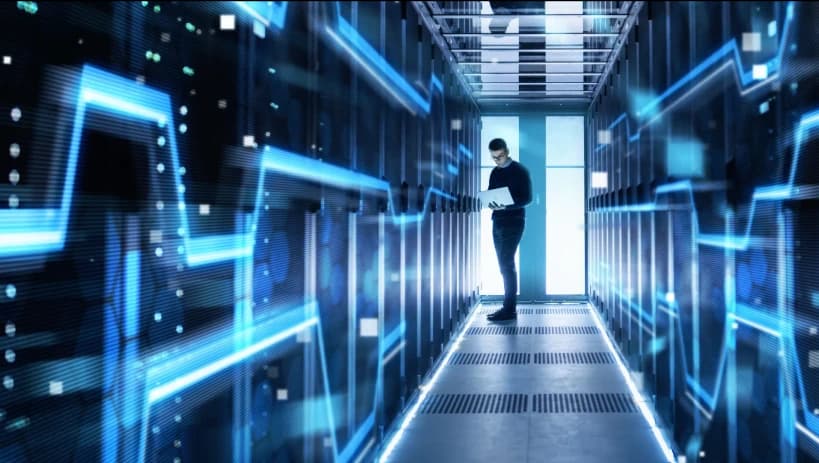 Specjalista IT pracujący na laptopie w futurystycznym centrum danych, otoczony oświetlonymi szafami serwerowymi i cyfrową grafiką sieciową, reprezentujący oparte na chmurze PLM (Product Lifecycle Management) i cyfrowe innowacje.